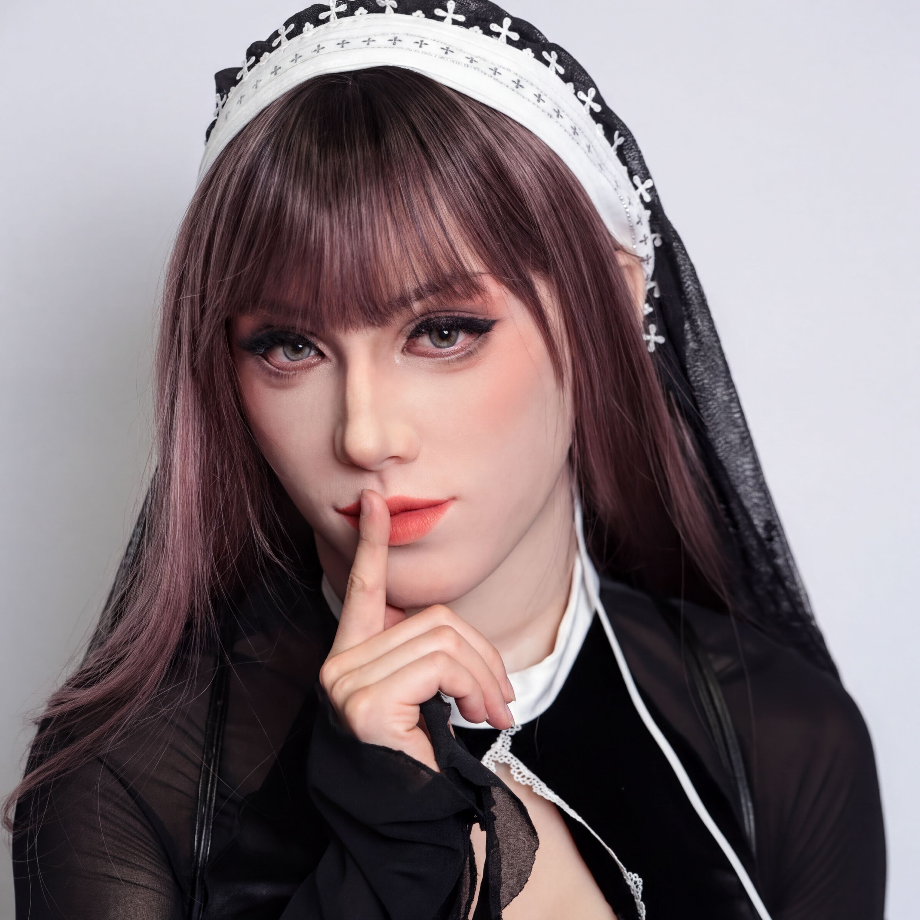 A woman with long brown hair wearing a black and white headband and a black dress poses with her finger on her lips.