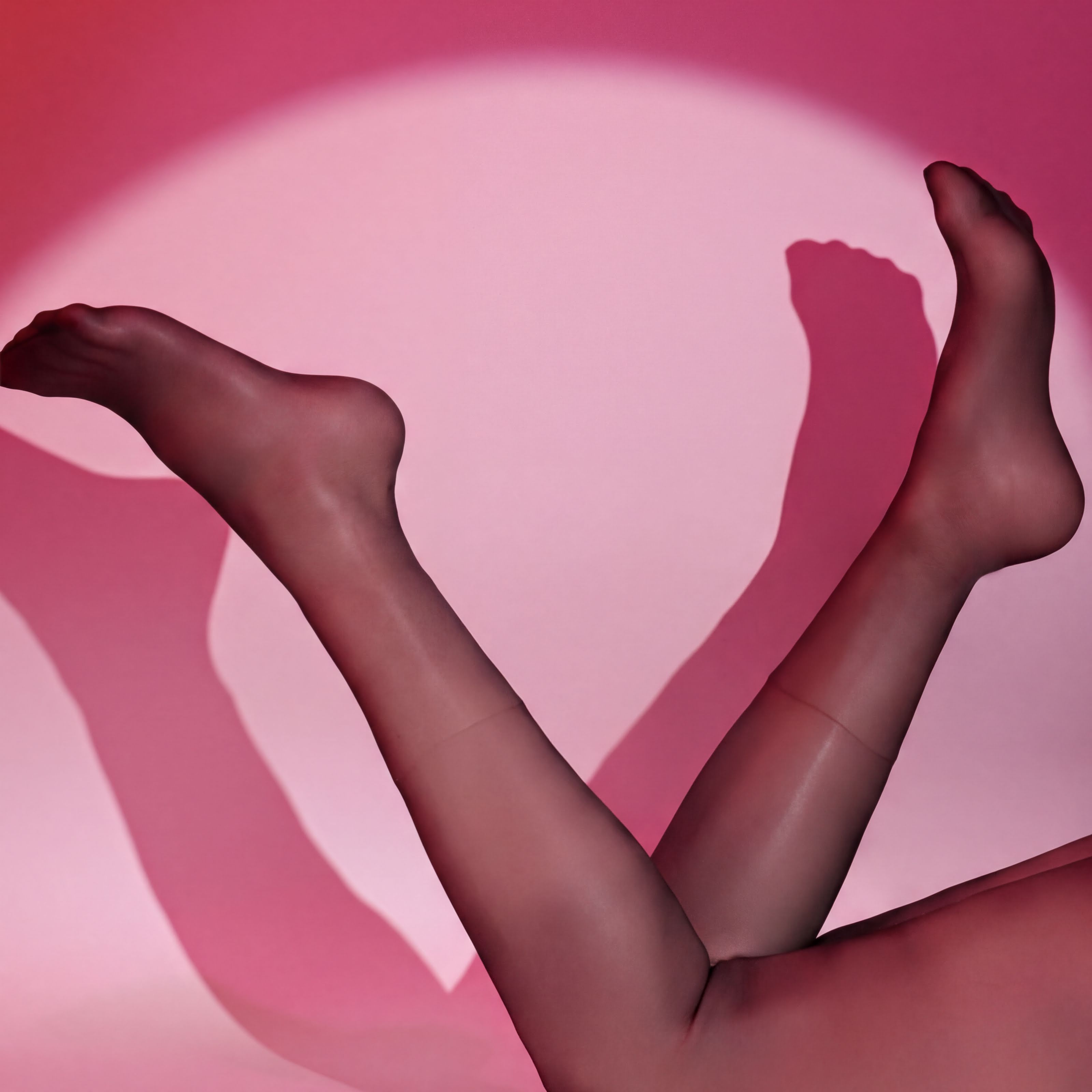 A close-up of a person's legs wearing sheer stockings against a pink background.