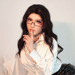 A woman with long dark hair wearing a white blouse and glasses is posing for a portrait.