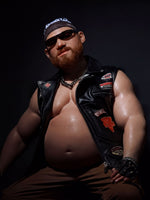 A muscular man wearing a leather jacket, sunglasses, and a bandana is posing for a portrait against a dark background.