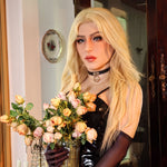 A woman with blonde hair is holding a vase of pink and white roses, wearing a black dress and a choker necklace.