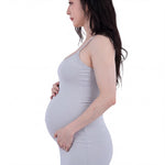 A pregnant woman with long dark hair stands with her hands on her stomach, wearing a gray tank top.